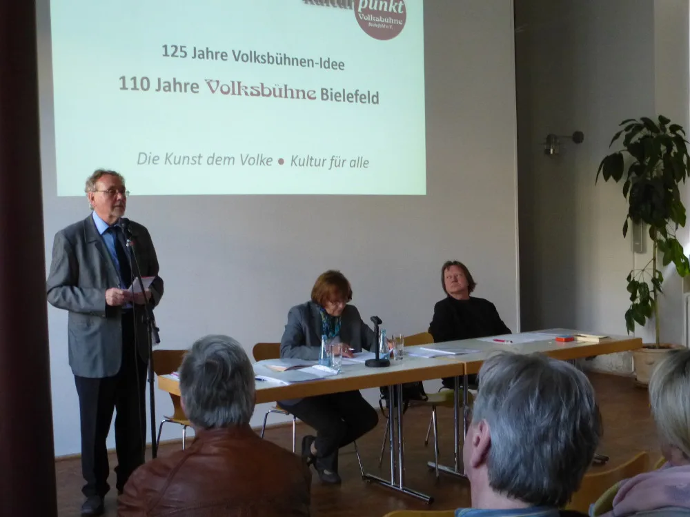 Redner bei der Mitgliederversammlung 2015 vor der Leinwand „110 Jahre Volksbühne Bielefeld“